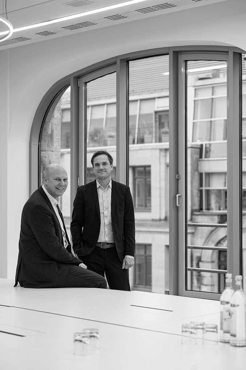Schwarz-Weiß-Porträt der Managing Partner von GSK Stockmann vor einem Rundbogenfenster
