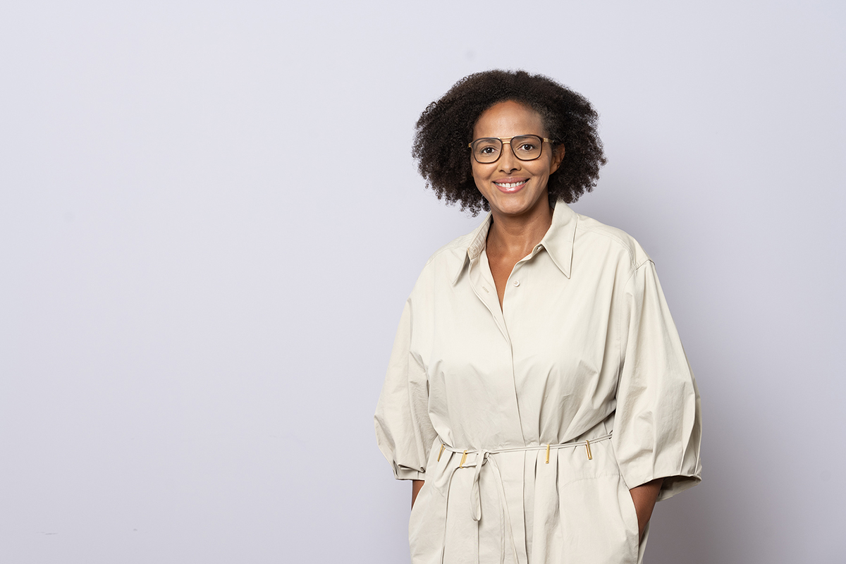 Natascha Thomas in schwarzer Bluse mit Brille, stehend vor hellem Hintergrund