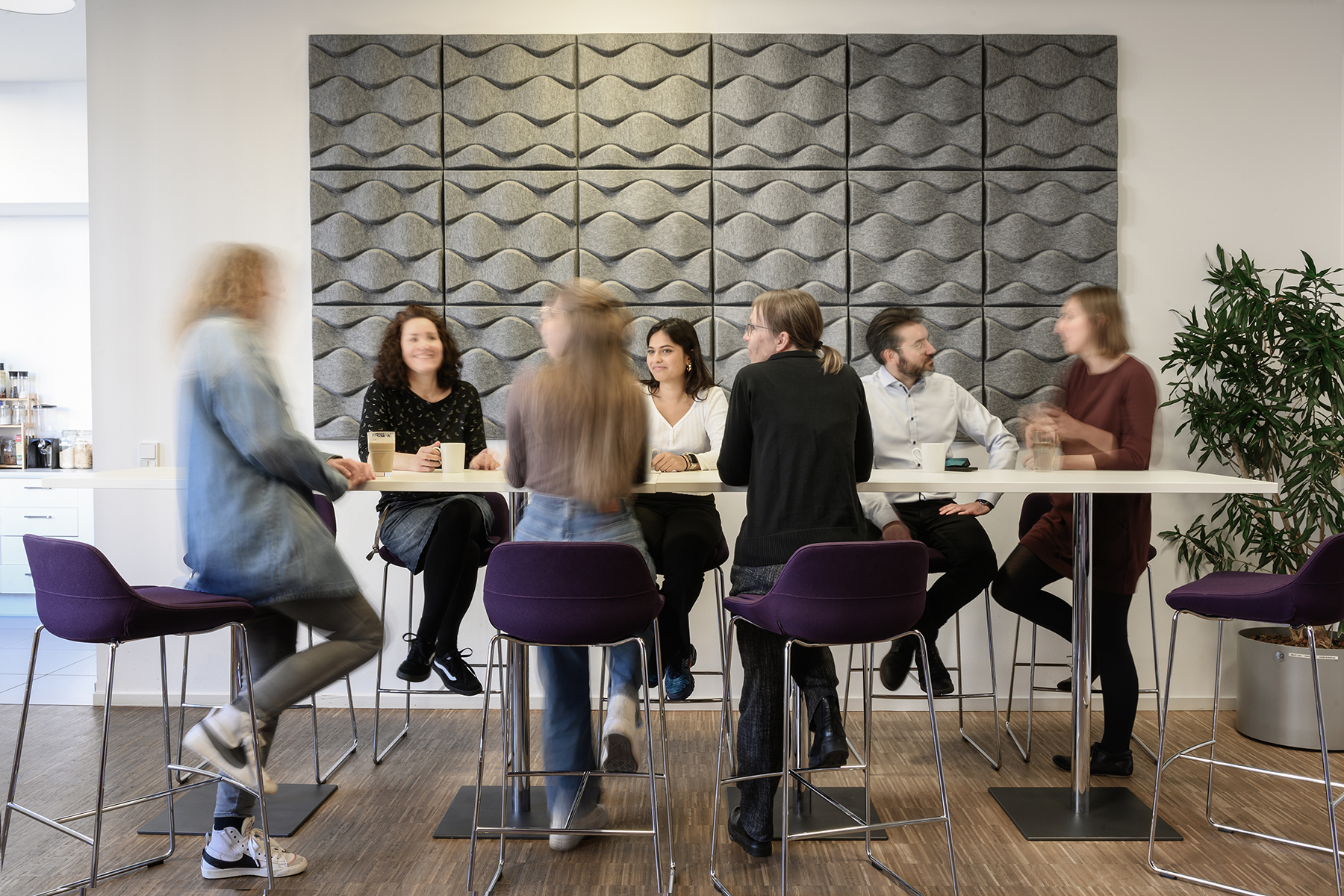 Team von GSK Stockmann im Gespräch an einem langen Stehtisch vor einer grauen Filzwand