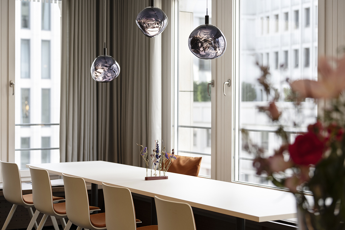 Besprechungsraum mit langem weißem Tisch, Glaspendelleuchten und Blumen im Vordergrund
