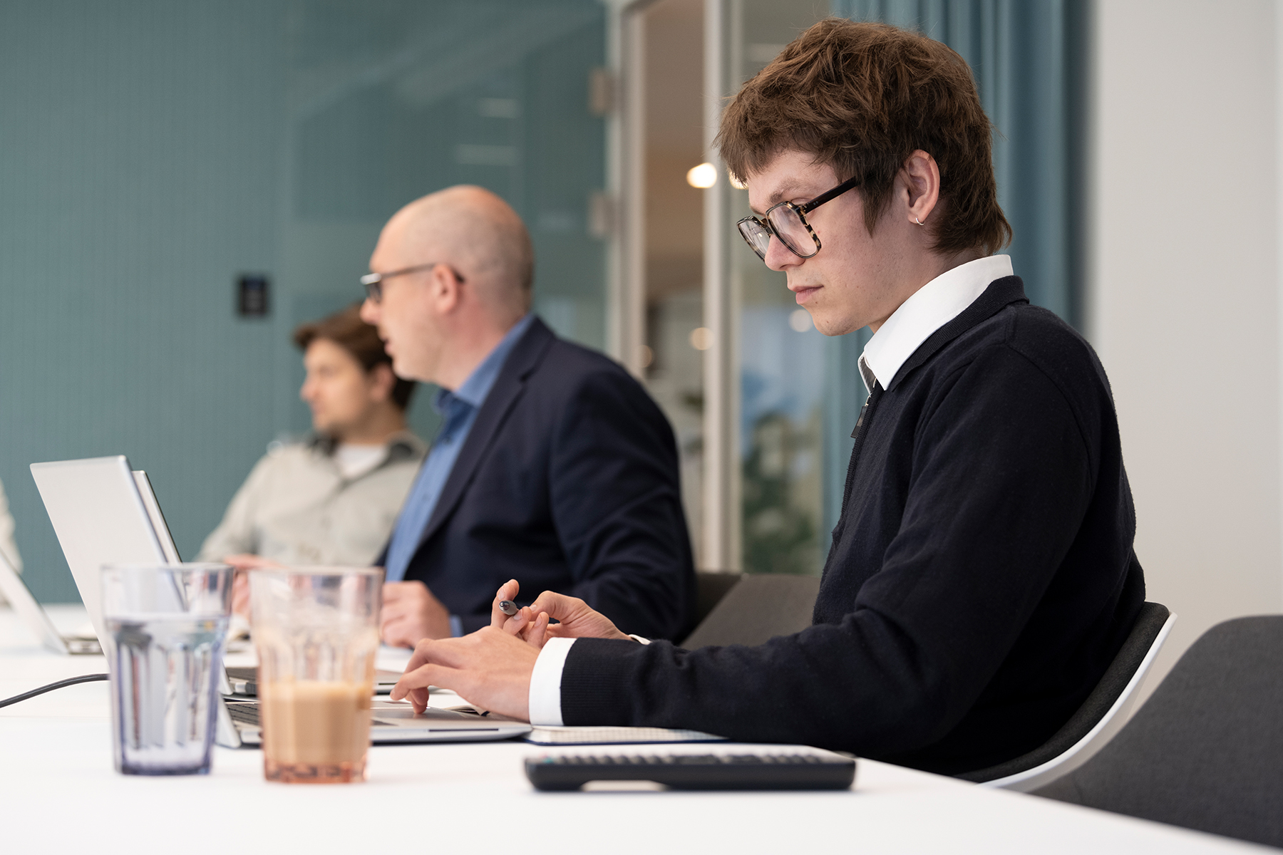 Drei Mitarbeitende von PMG Presse-Monitor arbeiten an Laptops an einem langen weißen Tisch