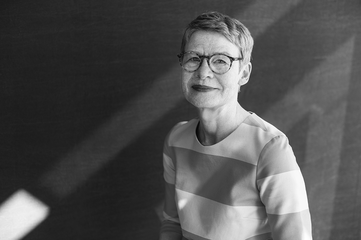 Schwarz-Weiß-Porträt von Regula Lüscher mit kurzem Haar und Brille vor einem Lichtstreifen